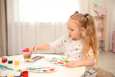 Cute little child painting at table in room