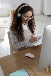 Photo of African American woman with headphones using modern computer for studying at home. Distance learning