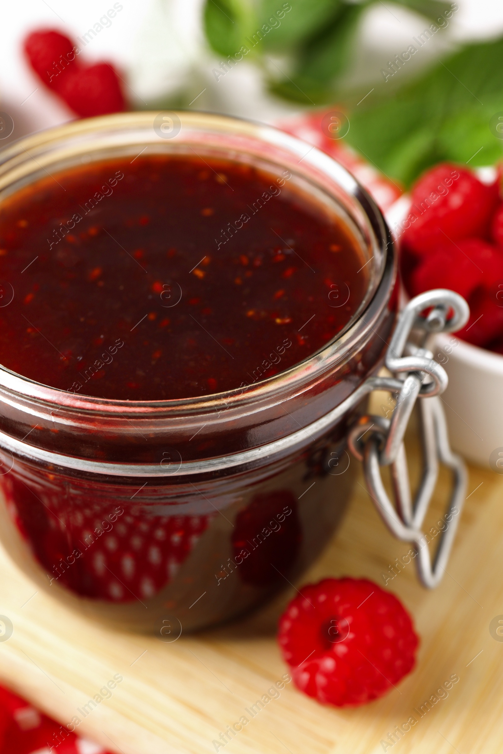 Photo of Jar of delicious raspberry jam and fresh berries on board, closeup