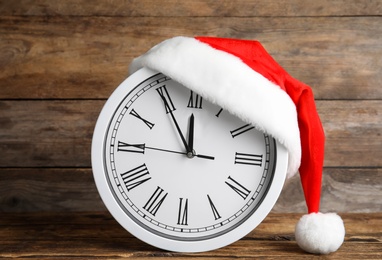 Photo of Clock with Santa hat showing five minutes until midnight on wooden background. New Year countdown