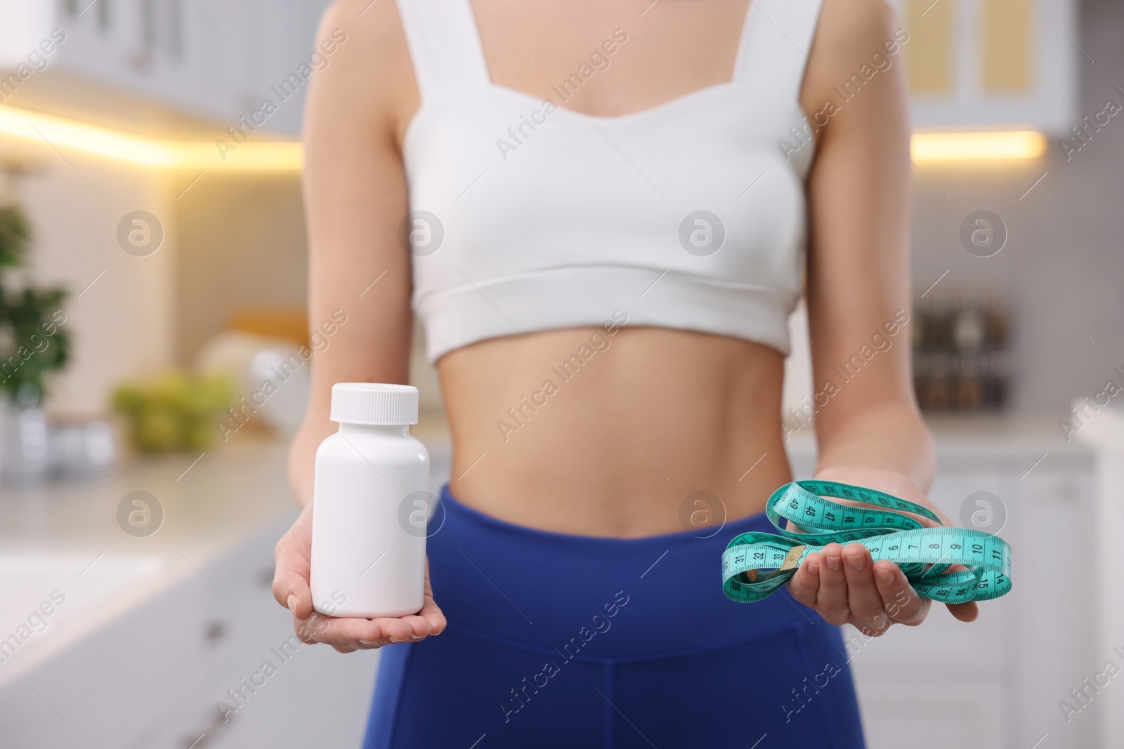 Photo of Woman with bottle of pills and measuring tape in kitchen, closeup. Weight loss