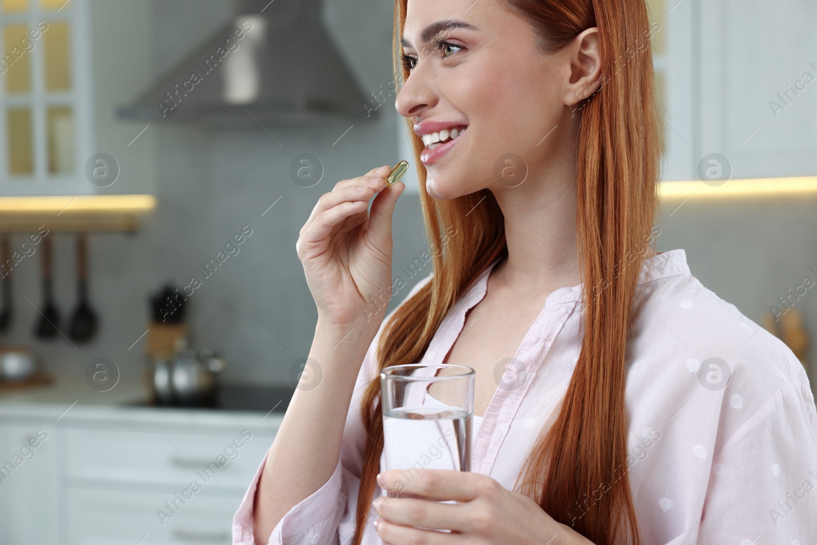 Photo of Beautiful young woman taking vitamin pill at home