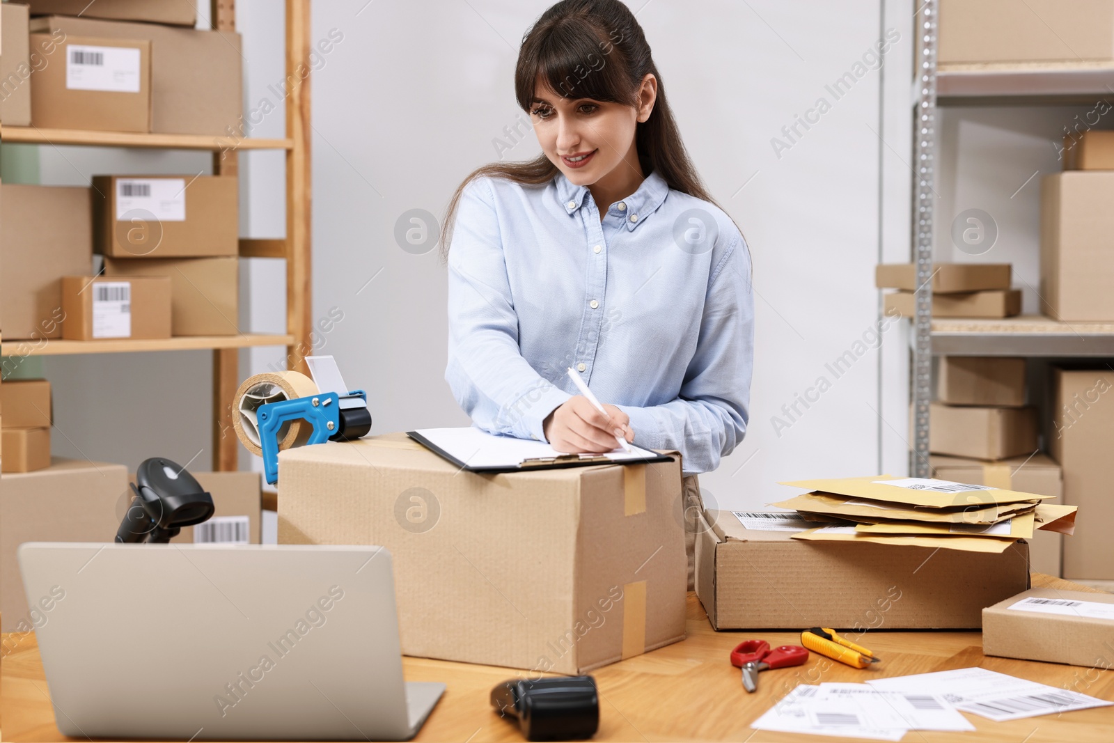 Photo of Parcel packing. Post office worker with clipboard writing notes at wooden table indoors