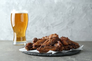 Photo of Delicious chicken wings and glass of beer on grey table