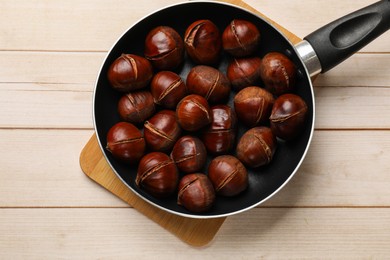 Roasted edible sweet chestnuts in frying pan on wooden table, top view