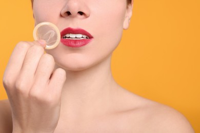 Photo of Woman holding condom on yellow background, closeup. Safe sex