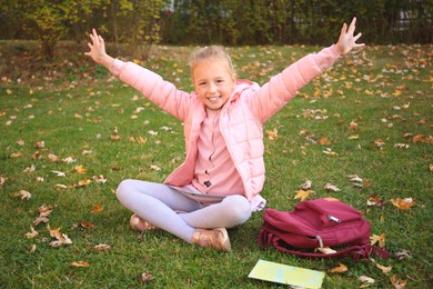 Cute little girl with copybook and backpack on green grass outdoors