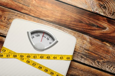 Photo of Weigh scales tied with measuring tape on wooden table, top view and space for text. Overweight concept