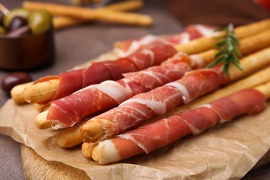 Photo of Delicious grissini sticks with prosciutto on table, closeup