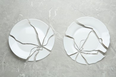 Photo of Two broken ceramic plates on light grey table, flat lay