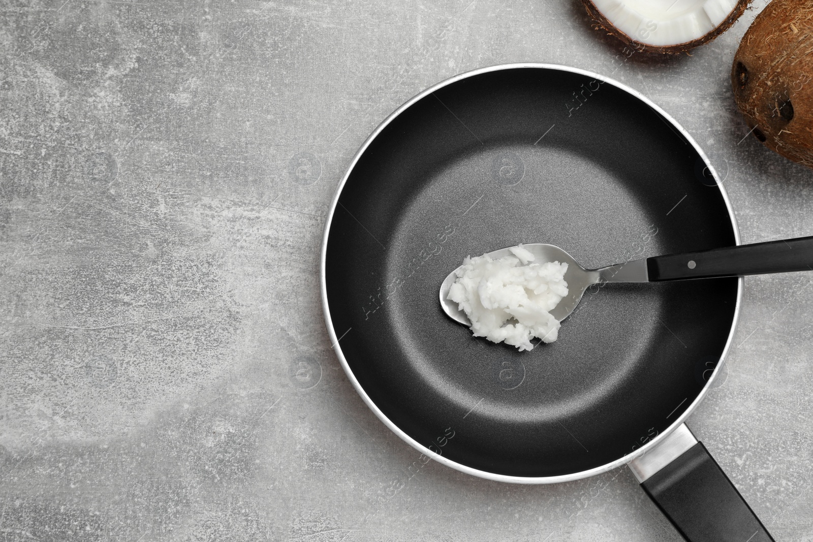 Photo of Frying pan with coconut oil and spoon on light grey table, flat lay. Space for text
