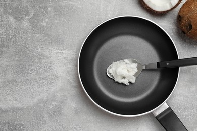 Frying pan with coconut oil and spoon on light grey table, flat lay. Space for text