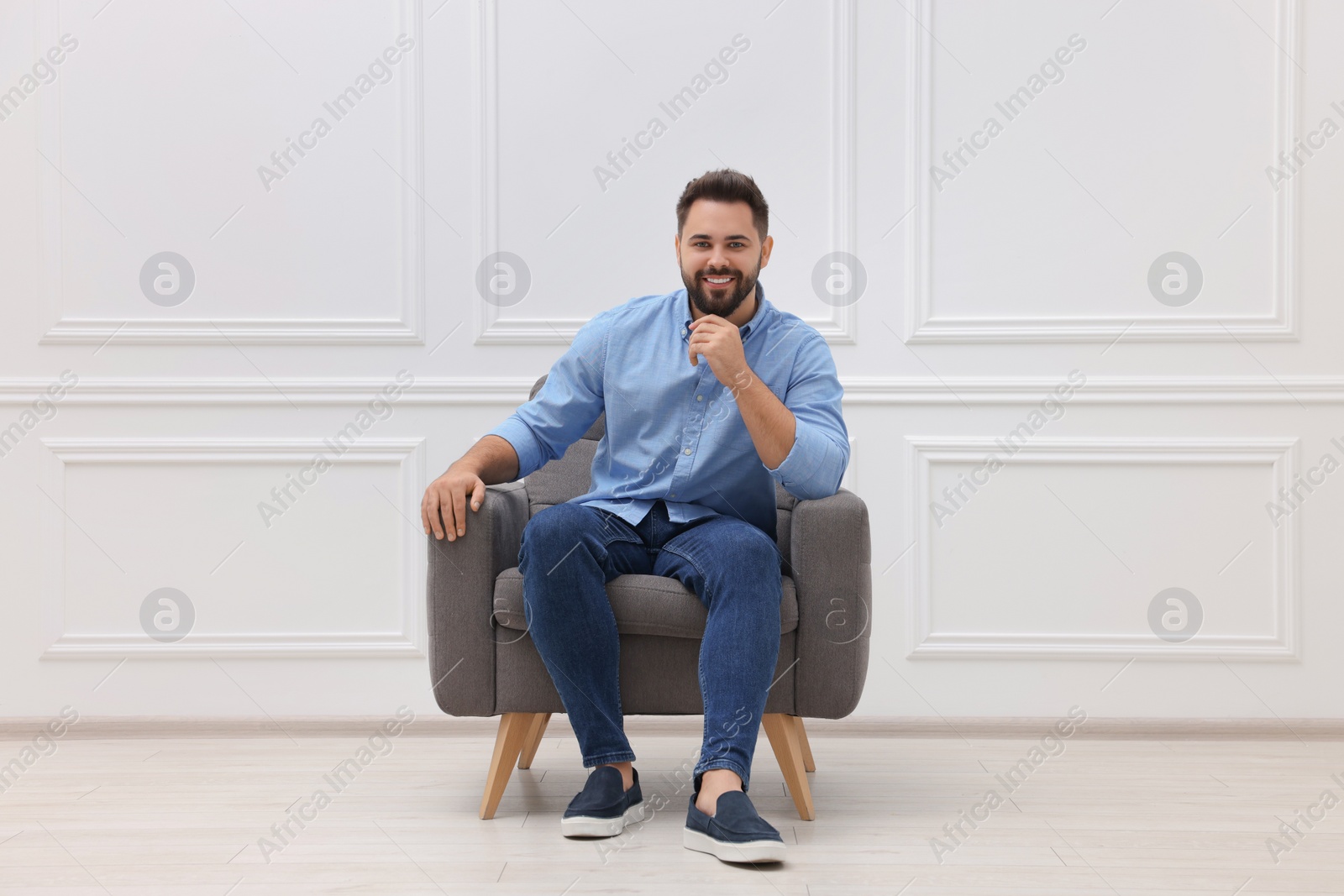 Photo of Handsome man sitting in armchair near white wall indoors