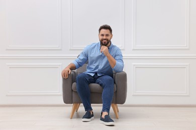 Photo of Handsome man sitting in armchair near white wall indoors