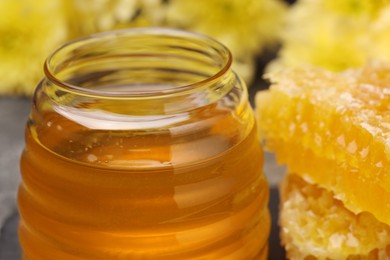 Sweet golden honey in jar and pieces of honeycomb on table, closeup