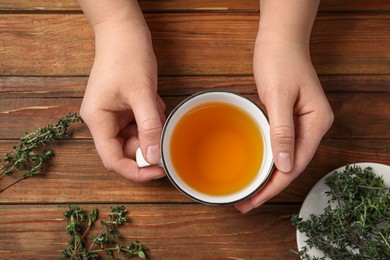 Photo of Woman with aromatic thyme tea at wooden table, top view