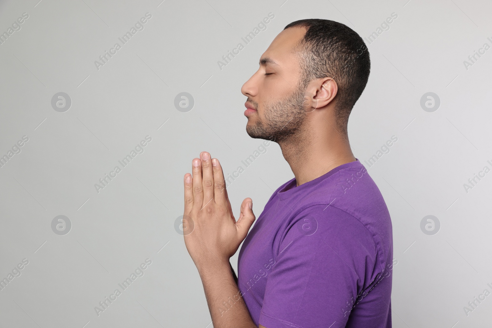 Photo of African American man with clasped hands praying to God on light grey background. Space for text