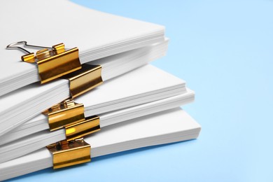 Photo of Many sheets of paper with golden clips on light blue background, closeup