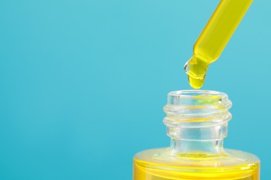 Dripping yellow serum from pipette into bottle on light blue background, closeup. Space for text
