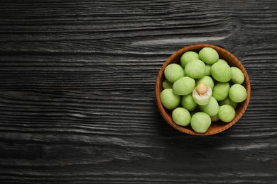 Tasty wasabi coated peanuts in bowl on black wooden table, top view. Space for text