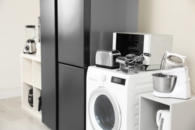 Photo of Modern refrigerator and other household appliances near beige wall indoors