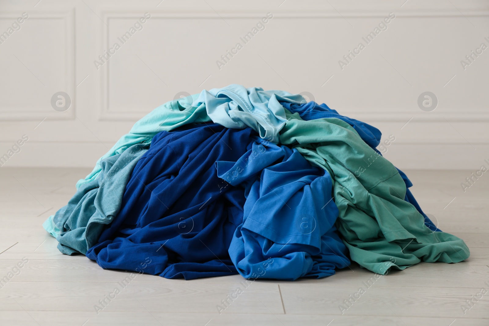 Photo of Pile of dirty clothes on floor near light wall indoors