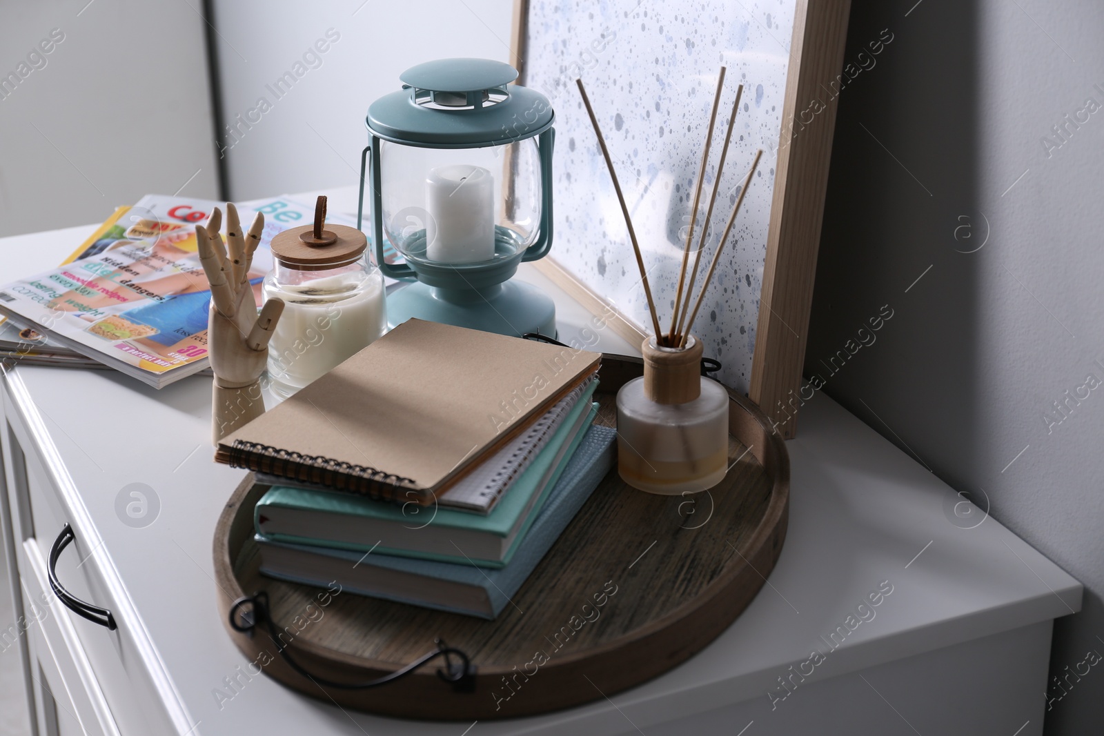 Photo of Wooden tray with notebooks, air reed freshener and decor on chest of drawers indoors