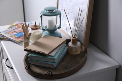 Photo of Wooden tray with notebooks, air reed freshener and decor on chestdrawers indoors