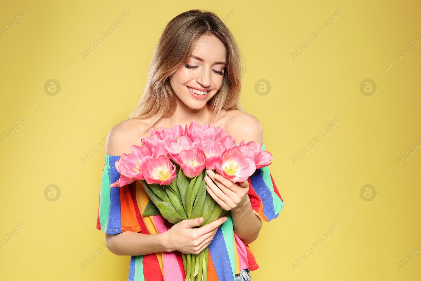 Photo of Portrait of beautiful smiling girl with spring tulips on yellow background. International Women's Day