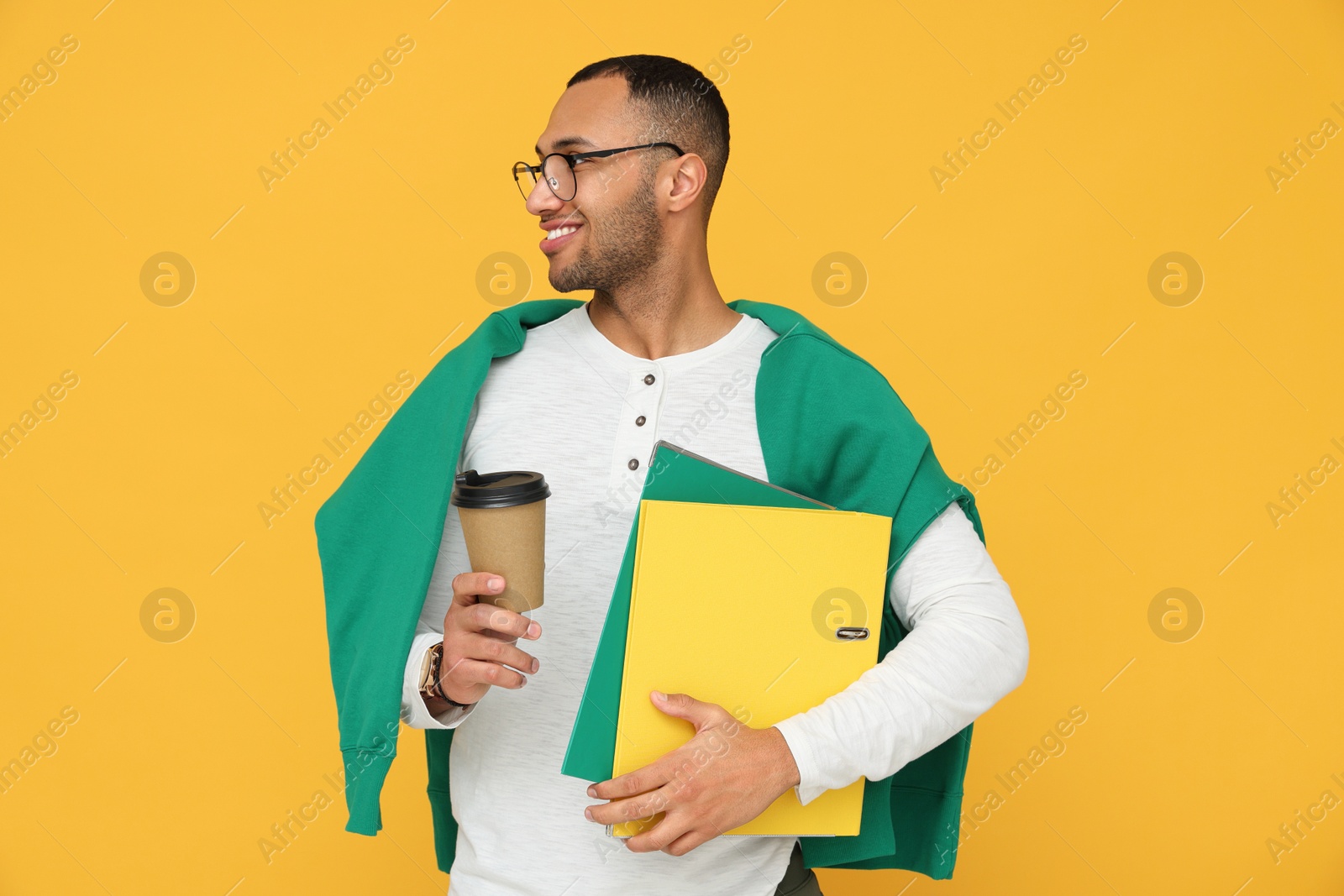 Photo of Happy young intern holding notebooks, cup of hot drink on orange background