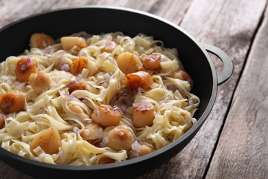 Photo of Delicious scallop pasta with onion in pan on wooden table, closeup