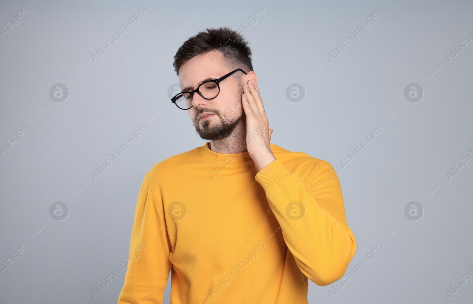 Photo of Young man suffering from ear pain on light grey background