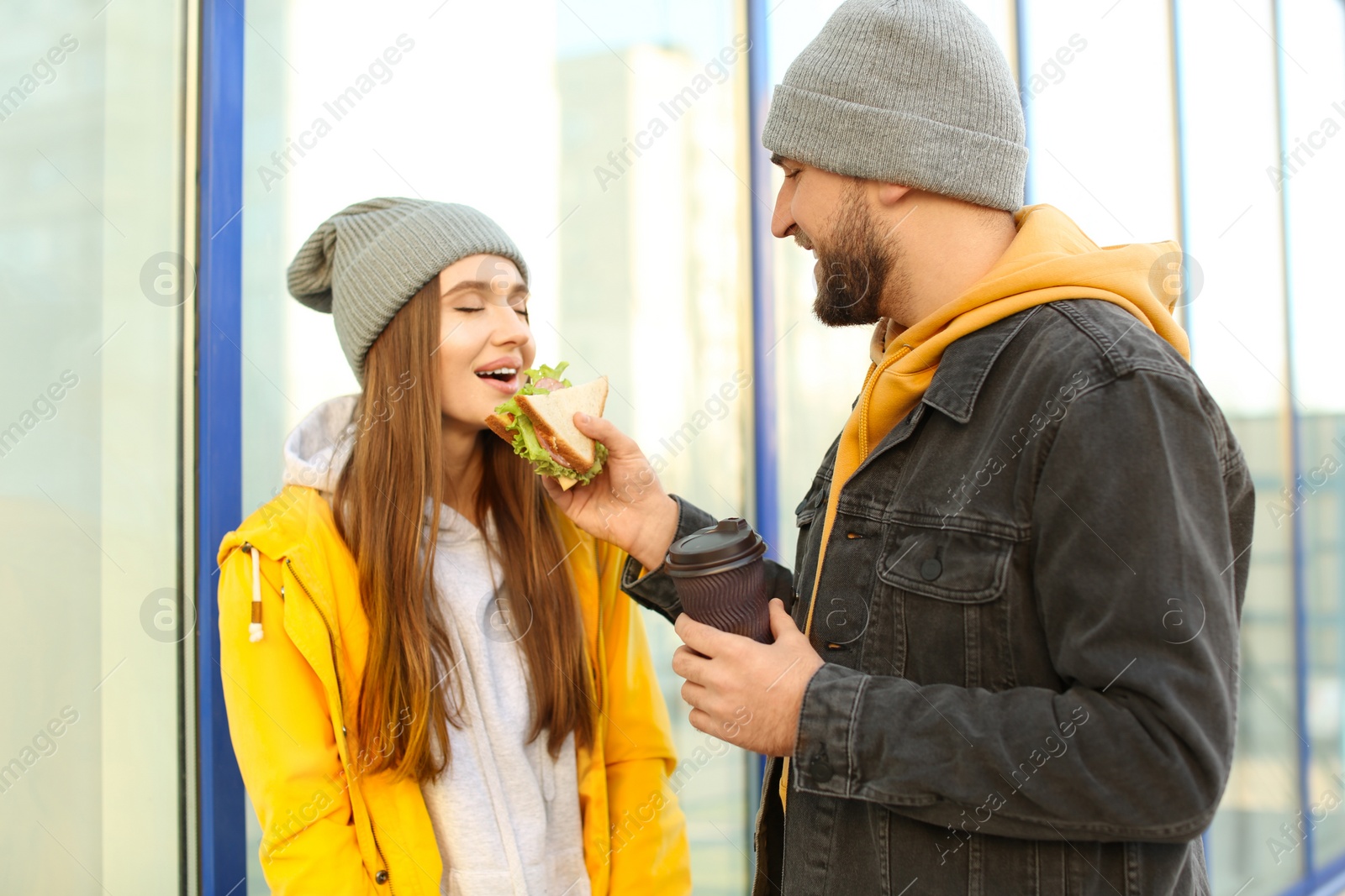 Photo of Cute young couple with sandwich and coffee on city street