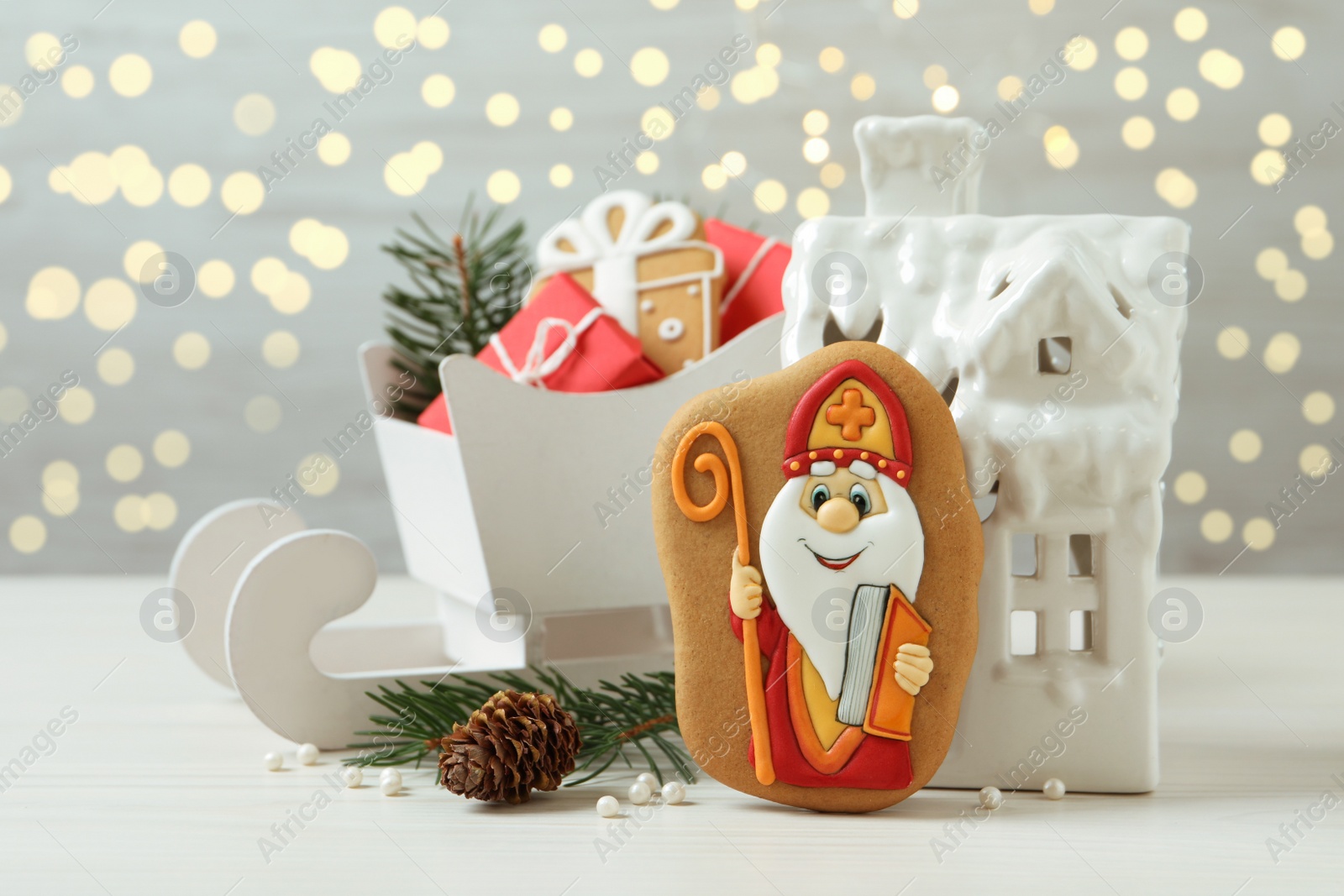 Photo of Composition with tasty gingerbread cookies on white wooden table against blurred lights. St. Nicholas Day celebration