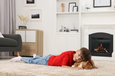 Photo of Little boy with cute ginger cat on soft carpet at home