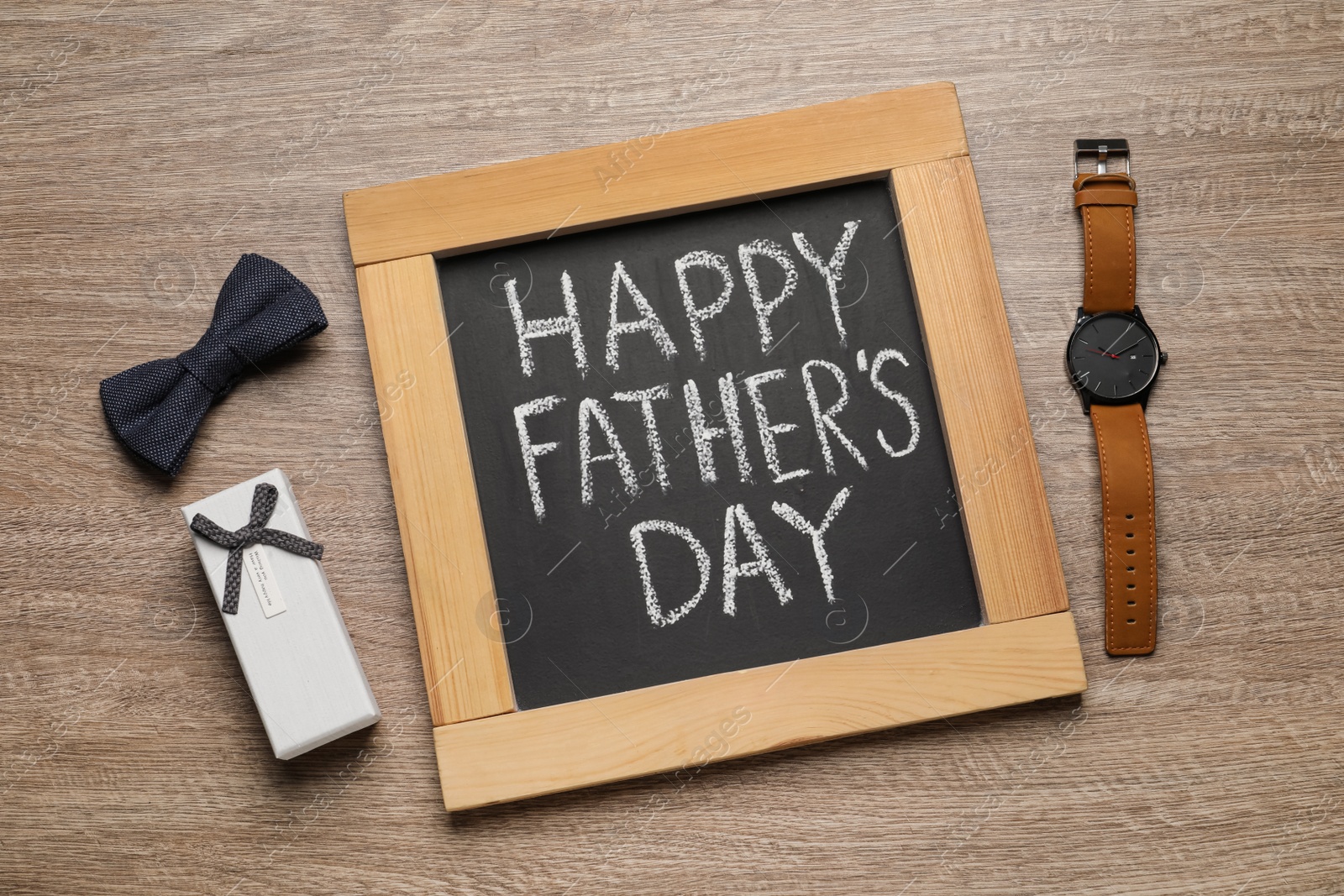 Photo of Chalkboard with phrase Happy Father's Day, gift box, wristwatch and bow tie on wooden background, flat lay