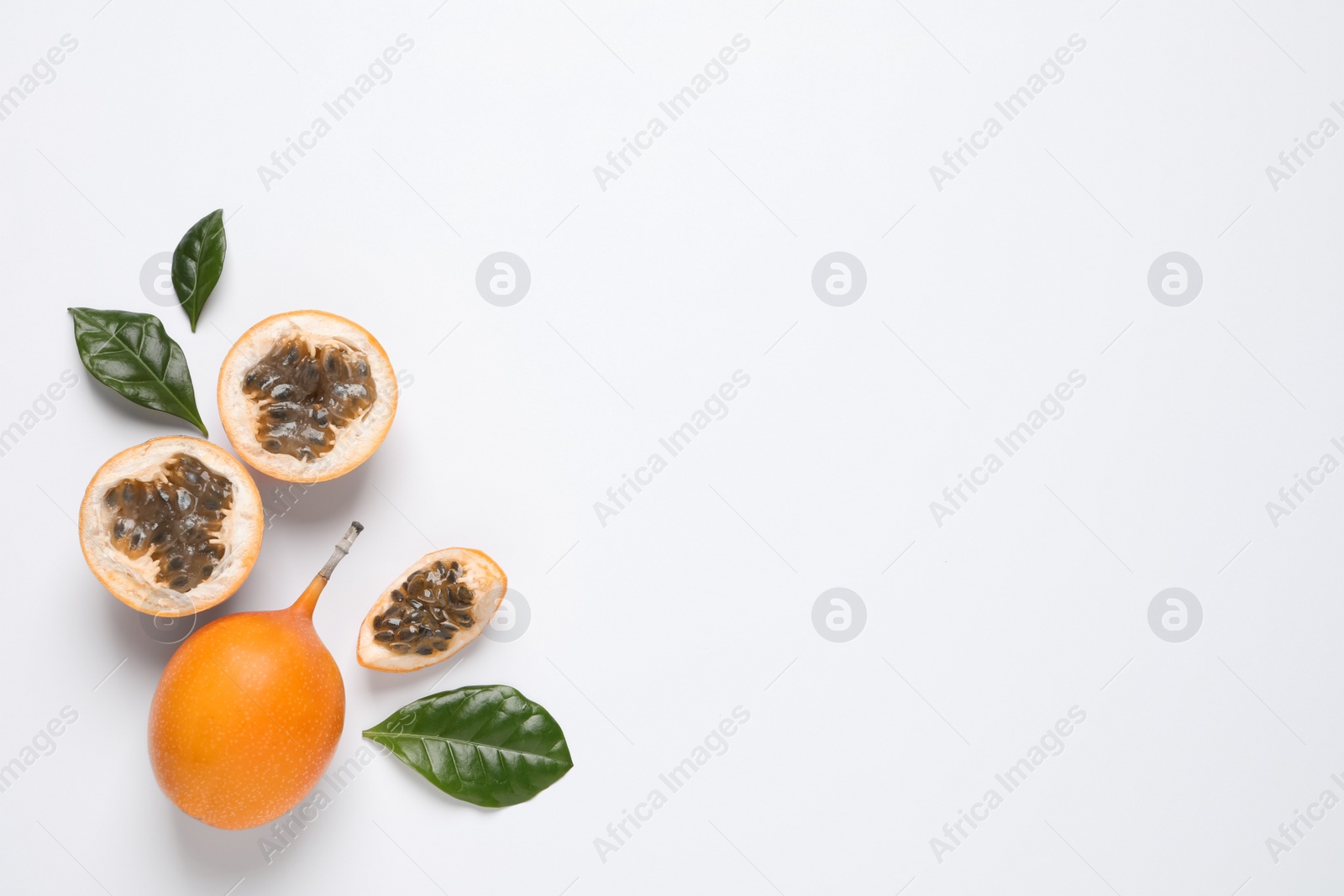 Photo of Delicious ripe granadillas with leaves on white background, flat lay. Space for text