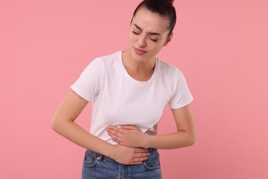 Woman suffering from abdominal pain on pink background. Unhealthy stomach