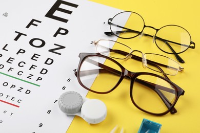 Vision test chart, glasses and lenses on yellow background, closeup