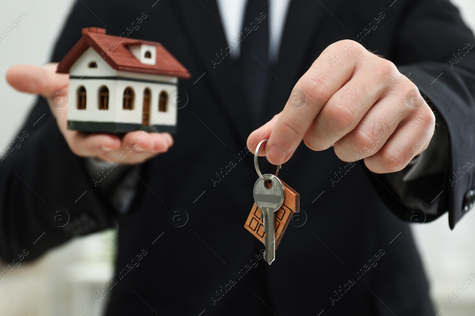 Photo of Real estate agent holding house model and key indoors, closeup