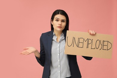 Unhappy woman holding sign with word Unemployed on pink background