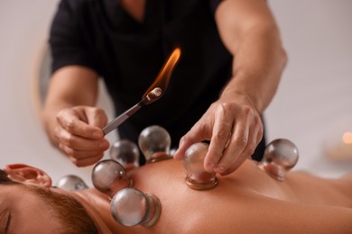 Photo of Therapist giving fire cupping treatment to patient indoors, closeup