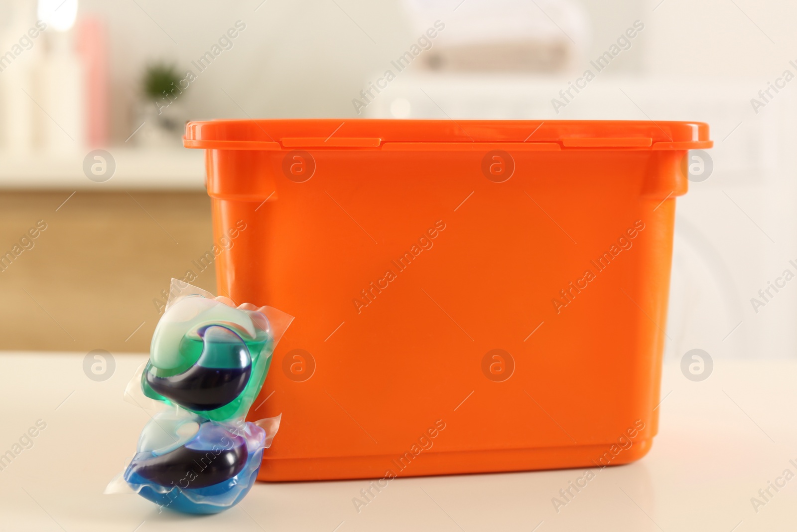 Photo of Laundry container and washing detergent capsules on table indoors