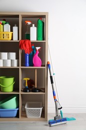 Photo of Shelving unit with detergents, cleaning tools and toilet paper near white wall indoors