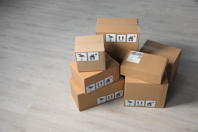 Photo of Many closed cardboard boxes with packaging symbols on wooden floor, space for text. Delivery service
