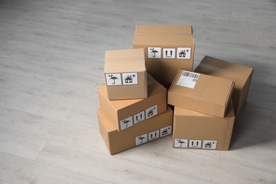 Many closed cardboard boxes with packaging symbols on wooden floor, space for text. Delivery service