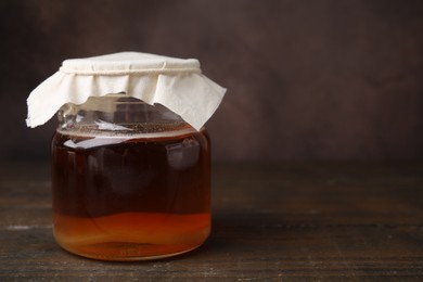 Photo of Tasty kombucha in glass jar on wooden table, space for text