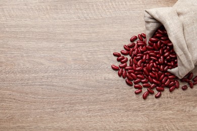 Photo of Raw red kidney beans with sackcloth bag on wooden table, flat lay. Space for text