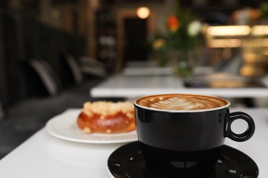 Photo of Cup of fresh coffee and bun on table in cafeteria