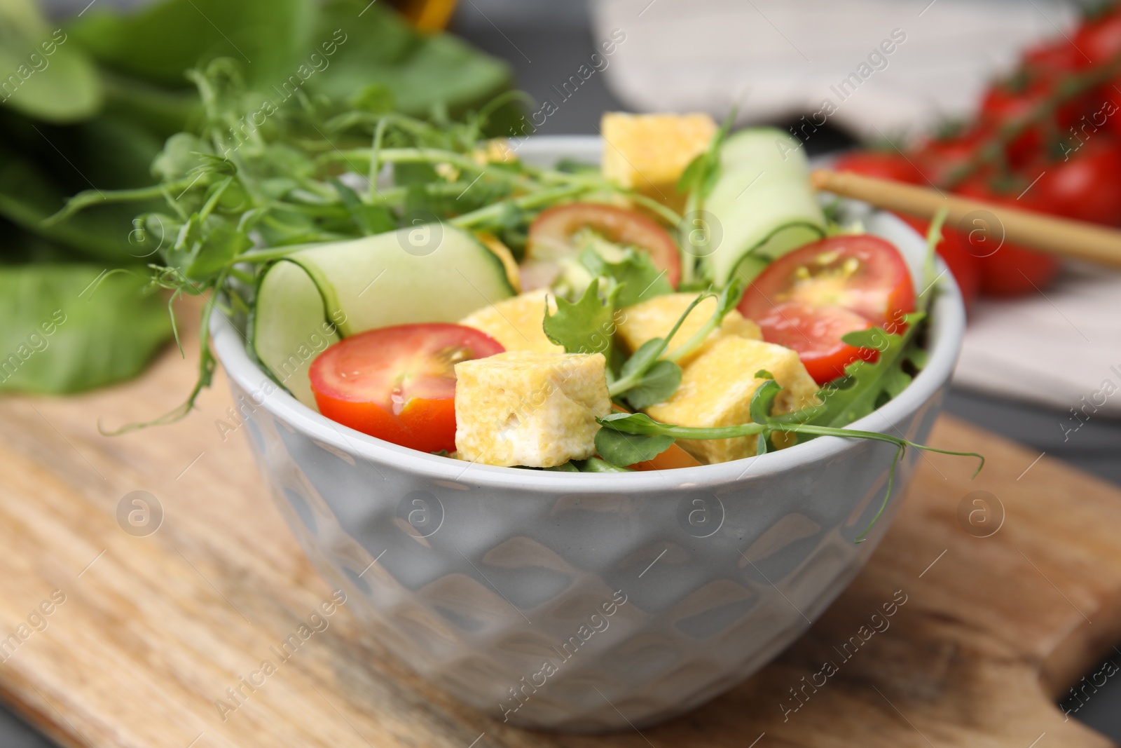 Photo of Bowl of tasty salad with tofu and vegetables on wooden board, closeup